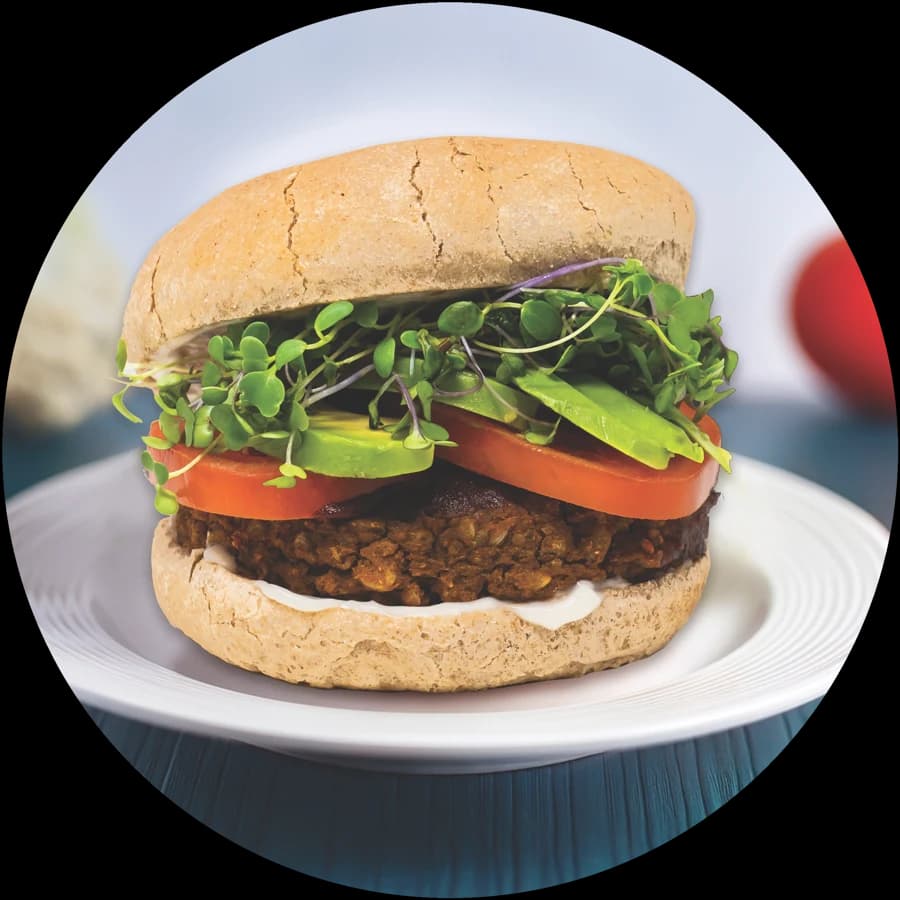 Yam black bean burger stacked with avocado, tomato and microgreens on a whole grain bun